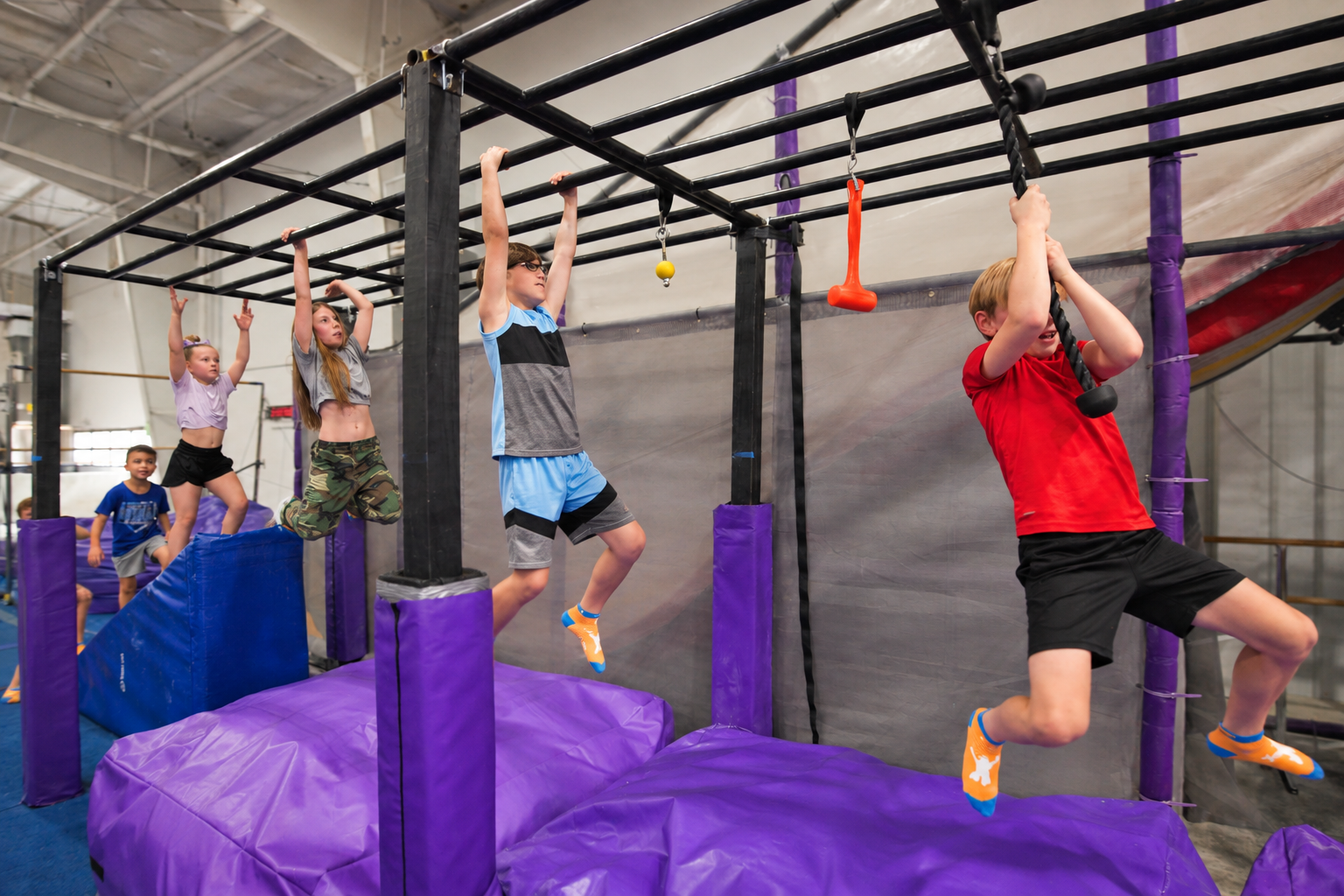 Children using the monkey bars and hanging obstacles above thick padding