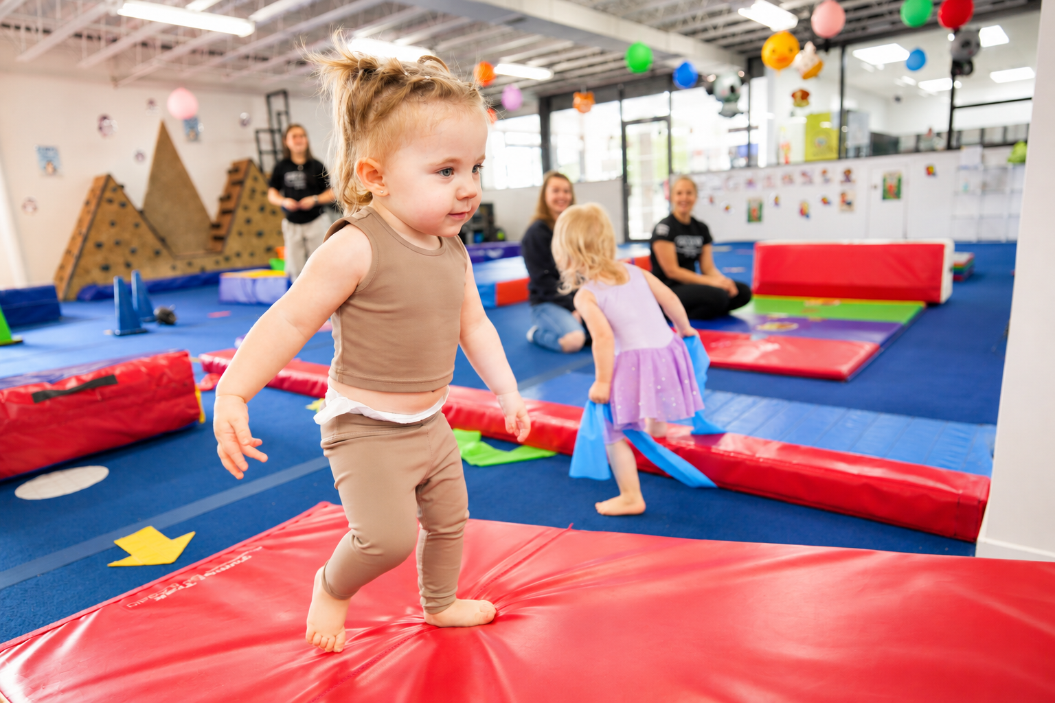 Toddler taking a small step on a padded mat with adults nearby